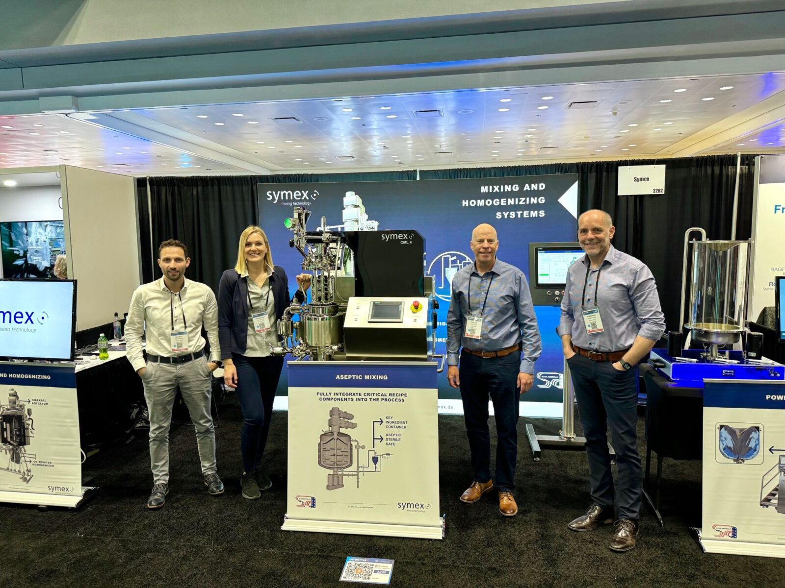 Tim Kruse (Scan American), Nico Sahr, and Daniela Ewert (symex) standing together at the symex booth during INTERPHEX 2025.