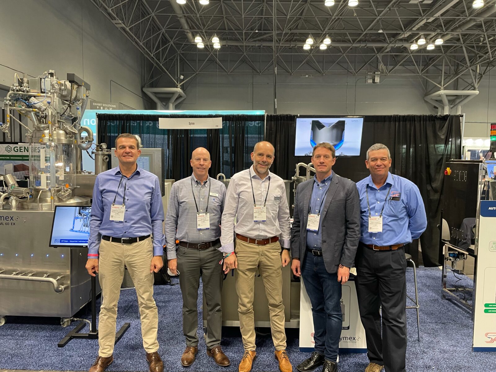 Group photo of the Scan American team with Ulf Sieckmann and Thorsten Panknin of symex in front of the symex booth at INTERPHEX 2021.