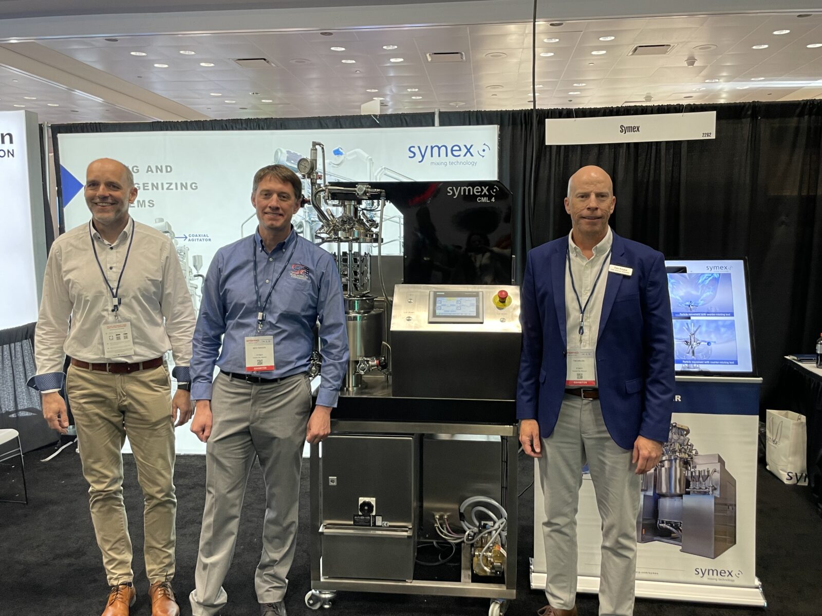 Ulf Sieckmann (symex) with Ben Parker and Tim Kruse (Scan American) standing in front of the symex booth at INTERPHEX 2023.